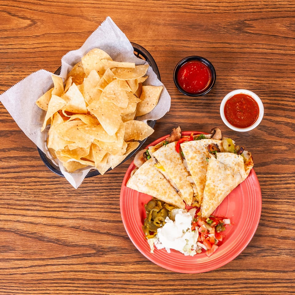 Quesadillas with jalapeños, sour cream, pico de gallo, tortilla chips, and salsa on a wooden table.