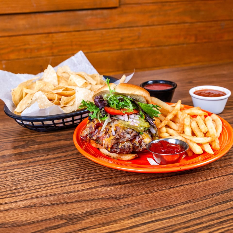 Loaded burger with cheese, bacon, and pulled pork, served with fries, ketchup, and tortilla chips.