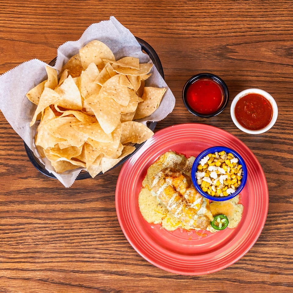 Shrimp dish with corn, jalapeños, tortilla chips, and two salsas on a wooden table.