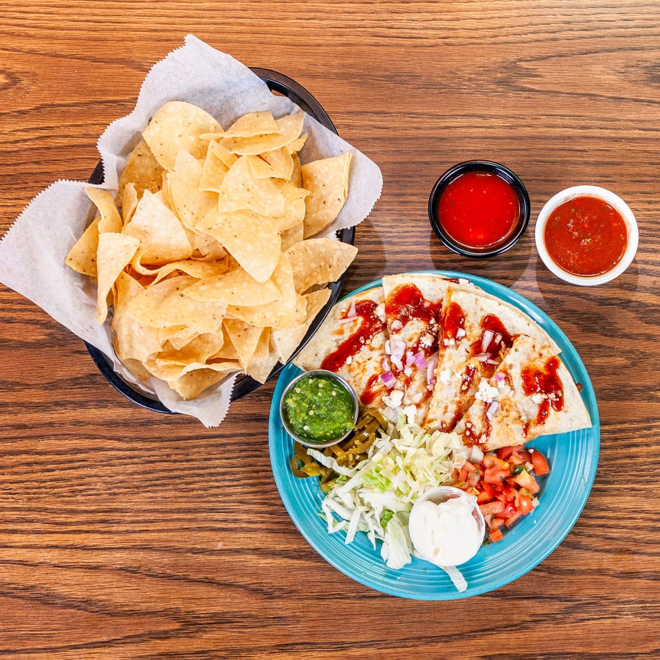 A plate of quesadillas with toppings, a basket of tortilla chips, and two bowls of salsa.